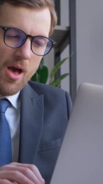 A tired manager is napping and yawning at work while using a laptop. Vertical video