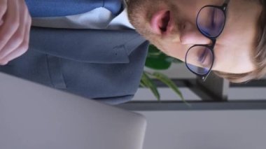 A tired manager is napping and yawning at work while using a laptop. Vertical video