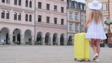 Bir turist kız bavuluyla turist evleri arıyor. Turizm yolculuğu yaşam tarzı. Güzel bir kadın sarı bir bavulla yürüyor..