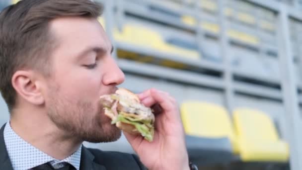 一个饿着肚子在公园里吃汉堡包的办公室工作人员在摄像机前的特写镜头 街头食品 — 图库视频影像