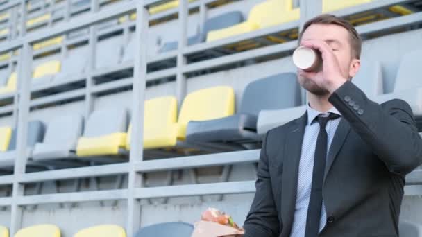Male Office Worker Eating Burger Drinking Coffee While Sitting Stadium — Stock Video