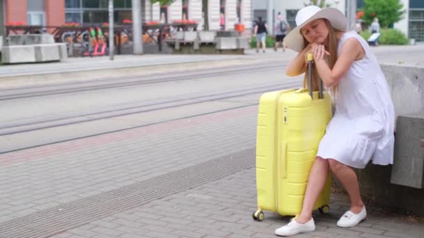 美しい女の子がスーツケースでバス停に座っている トラムを待っている間荷物で寝ている疲れた観光客の女性 — ストック動画