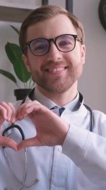 Doktor kameraya bakarak kalp hareketini ve gülüşünü gösterir. İnsanları tedavi etme kavramı. Dikey video