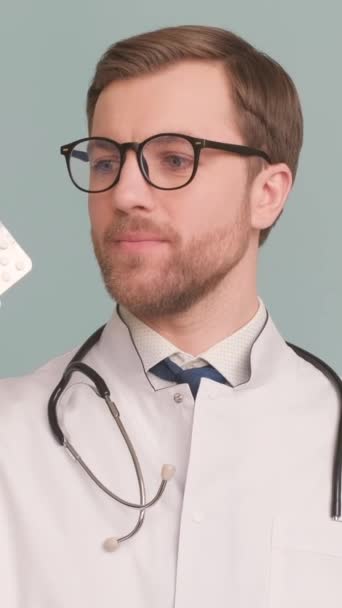 眼鏡のスタイリッシュな医者は錠剤を示し それらをお勧めしません スタジオの背景にある医師の肖像画 バーティカルビデオ — ストック動画