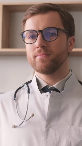 白いコートと眼鏡の医者の肖像画 彼はカメラを見て微笑んでいる 医学の概念 バーティカルビデオ — ストック動画