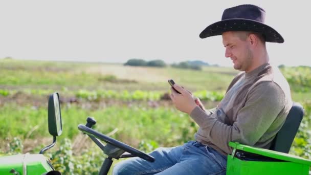 果樹園で屋外でミニトラクターを運転する若い農夫は スマートフォンを使用しています フィールドの農学者 — ストック動画