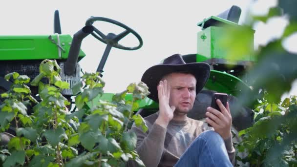 Wściekły Rolnik Rozmawiający Przez Telefon Siedzący Przed Zielonym Ciągnikiem Terenie — Wideo stockowe