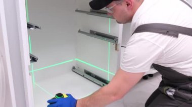 Mutfak dolabına bir çekmece yerleştirmek için lazer seviyesi kullanan bir adam. Daire yenileme konsepti.