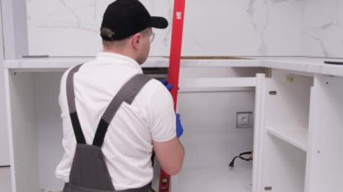 Üniformalı bir usta inşaat seviyesini kullanarak mobilya kuruyor. Aksesuarların kurulumu.