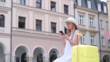 Genç bir bayan turist şehir merkezinde bir bavulun yanında otururken akıllı telefon kullanır. Seyahat ve turizm kavramı