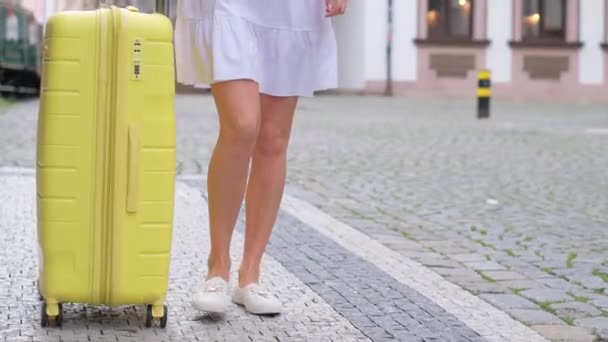 若い女性旅行者が街中を黄色いスーツケースで歩いています フロントビューを閉じる — ストック動画