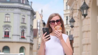 Güzel bir bayan turist sokakta yürüyor ve lezzetli bir Fransız kruvasanı yiyor. Seyahat kavramı