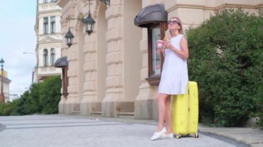 Genç, şık bir turist kahve ve kruvasanla Fransız kahvaltısı yapıyor. Dışarıda bavulun üzerinde oturuyor. Avrupa seyahatleri