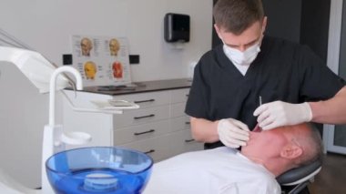 Genç bir erkek dişçi yaşlı bir hastanın dişinin sağlığını izler. Diş tedavisi prosedürü. Bir dişçinin işi.