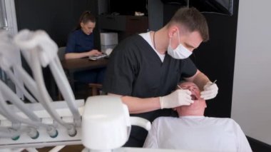 Yaşlı gri saçlı adam dişçi koltuğunda oturuyor, doktor özel diş aletleriyle bakımı yapıyor, doktor çok profesyonel çalışıyor..