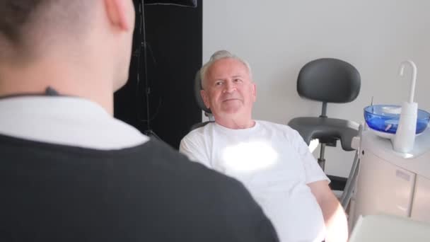 一位老年人坐在牙医办公室的牙椅上 他正在和一位医生谈话 牙科治疗概念 — 图库视频影像