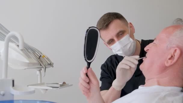 Młody Dentysta Masce Ochronnej Pracuje Starszym Pacjentem Klinice Lekarz Pokazuje — Wideo stockowe
