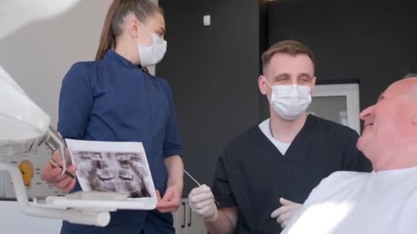 Büyükbaba Dişçi Koltuğunda Oturuyor Doktor Diş Röntgenlerini Gösteriyor Diş Protezlerinin — Stok video