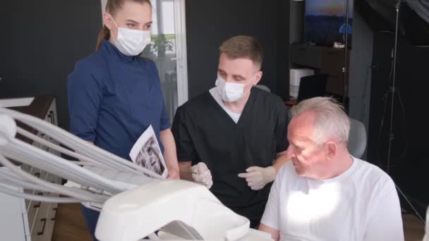 一位老人坐在牙椅上听牙医讲话 为养恤金领取者植入牙齿 — 图库视频影像