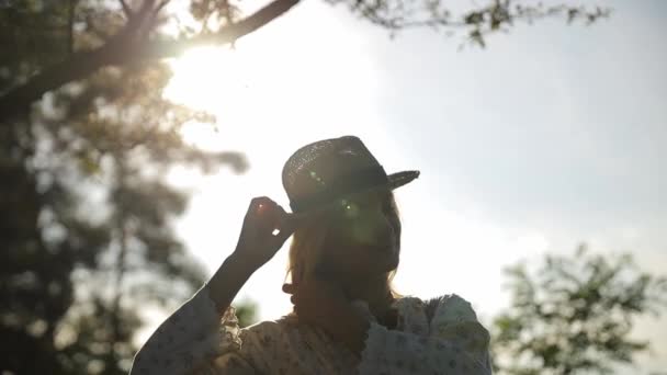 森の中央の太陽の光線の背景に対する帽子の美しい女の子のシルエット スローモーション — ストック動画