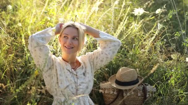一个年轻的金发女子坐在高高的草地上欣赏日落 女人是天生的 — 图库视频影像