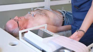 Deneyimli kadın teşhis uzmanı genç bir hastaya kardiyogram çekiyor. Elektrokardiyogram. Hastaların EKG 'sini al..