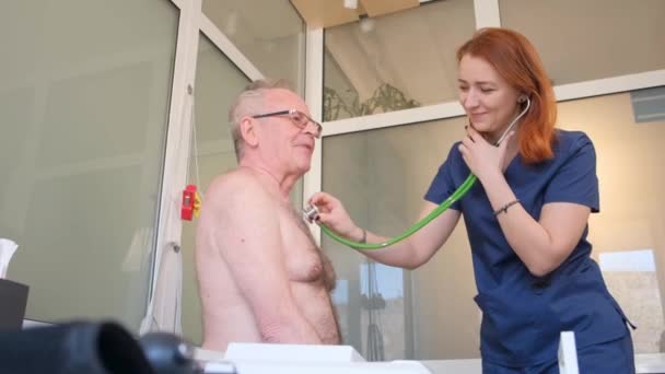 医師は 心臓のリズムをステートスコープで診察する 心臓専門医事務所で高血圧を患っている患者 — ストック動画