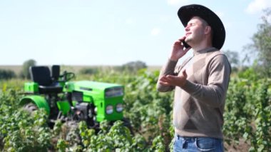 Tarlada traktörün önünde cep telefonuyla konuşan mutlu genç çiftçi..