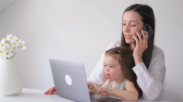 商业母亲和她的小女儿在家里工作 没有临时保姆 工作的母亲坐在白墙旁边 一边打电话一边聊天 — 图库视频影像