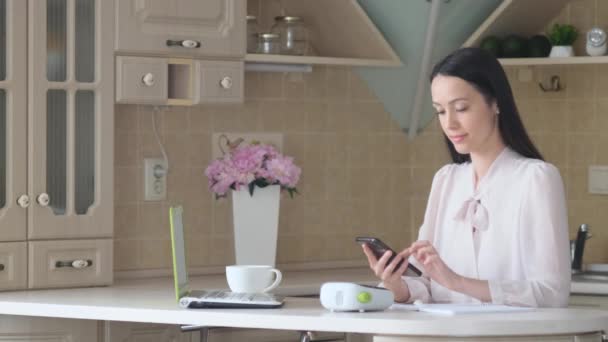 Dizüstü Bilgisayarda Çalışan Güzel Bir Esmer Mutfakta Cep Telefonu Kullanıyor — Stok video