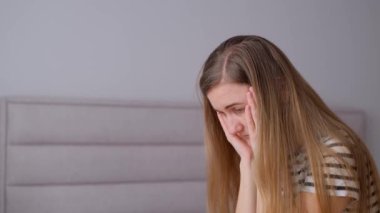 Mutsuz, uzun saçlı genç bayan sabahları yatakta oturuyor, tapınakları ovuyor, aşağı bakıyor, baş ağrısı çekiyor..