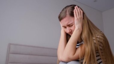 Yatakta oturan genç bir kadının başı ağrıyor. Migren, yorgunluk, depresyon..
