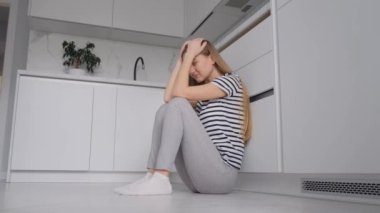 Depresyondan muzdarip genç bir kadın mutfakta yerde oturuyor. Ruh sağlığı sorunları.