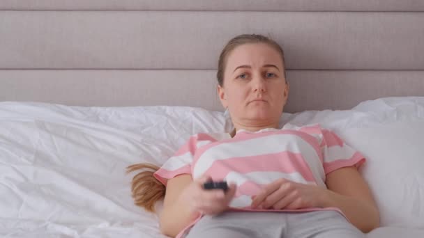 ベッドの上に横たわっている少女がリモートコントロールを使用してチャンネルを切り替えます — ストック動画