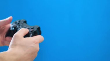 Mavi arka planda oyun konsolunda oynayan bir adamın elleri. Bir joystick kullanarak bilgisayar oyunları.