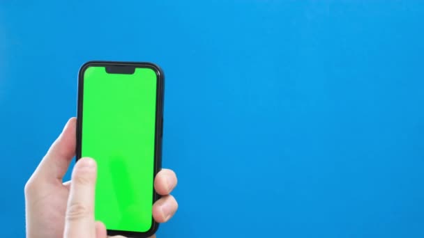 青い背景の緑のスマートフォン画面 スマートフォンを使用したハンドのクローズアップ クロマケイの背景 — ストック動画