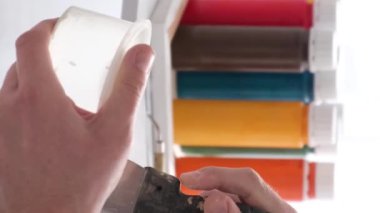 Kapatın. Ressamların eli, kaptaki beyaz boyayı spatulayla karıştırır. Beyaz tonlarda yaratıcı atölye çalışması. Bir resim yaratma süreci. Fırça hareketi. Dikey video