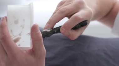 Sanatçı ayağa kalkar ve beyaz boyayı bir spatulayla karıştırır. Beyaz tonlarda yaratıcı atölye çalışması. Bir resim yaratma süreci. Fırça hareketi. Dikey video