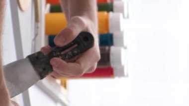 Kapatın. Ressamların eli, kaptaki beyaz boyayı spatulayla karıştırır. Beyaz tonlarda yaratıcı atölye çalışması. Bir resim yaratma süreci. Fırça hareketi. Dikey video