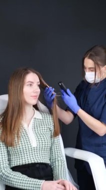 Bir trikoloğun muayenesi. Doktor fotoğraf çeker, genç bir kızın saç yapısını tarar. Saç makroskopisi. Güzellik kliniği. Dikey video