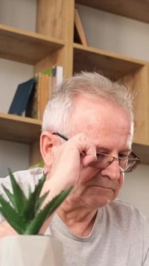 Yorgun büyükbabam dizüstü bilgisayarda çalışıyor, başı ağrıyor, başını kucaklıyor. Yaşlı bir adamın migreni. Dikey video