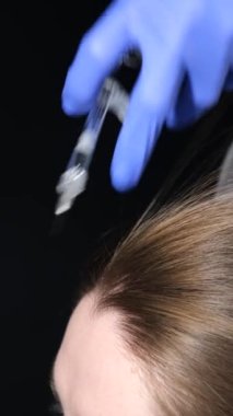Tıbbi eldivenli bir trikoloğun kadına saç dökülmesine karşı iğne yapması. Kafa derisindeki hastalıkların tedavisi. Dikey video