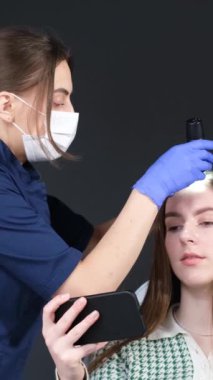 Saç trişoskopisi prosedürü. Bilgisayar trikoskopisi. Bir trikoloğum klinikte trikop kullanarak hastaların saçlarını inceliyor. Dikey video