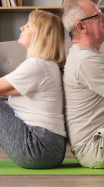 Büyükannem ve büyükbabam fitness paspasları üzerinde otururken meditasyon yapıyorlar. Yoga egzersizleri. Emeklilikte sağlıklı bir yaşam tarzı. Dikey video