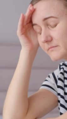 Çekici genç bir kadın evindeki kanepede oturuyor, baş ağrısı çekiyor, yorgun ve endişeli ve depresyondan muzdarip. Dikey video