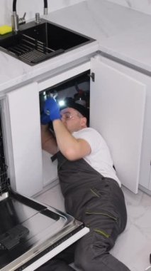 Mutfakta yerde yatan bir tesisatçı lavabo yerleştirir. Tesisatçı işi. Dikey video