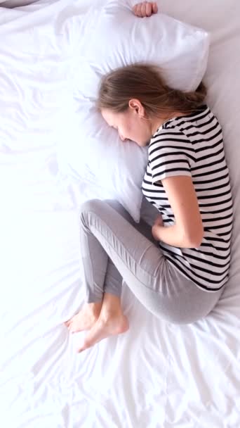 病重的年轻妇女躺在床上 忍着肚子 严重的胃痛下毒了月经期疼痛 垂直录像 — 图库视频影像