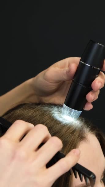 バーティカルビデオ フラッシュライトとコムを使用したトリコロジストによる患者の頭皮の検査 美容クリニックで バーティカルビデオ — ストック動画