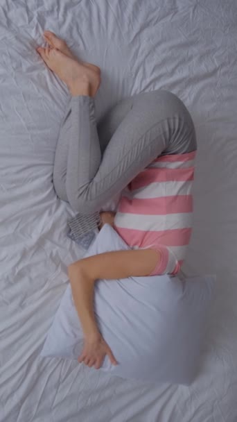 若い女性がベッドの上に横たわり 月経中に腹痛に苦しんでいます 鎮痛剤を服用する バーティカルビデオ — ストック動画