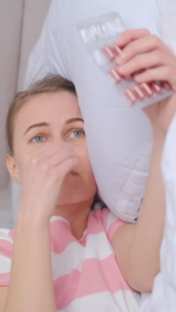 若い女性がベッドの上に横たわり 月経中に腹痛に苦しんでいます 鎮痛剤を服用する バーティカルビデオ — ストック動画
